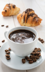 two croissants and a cup of coffee on a white wooden table