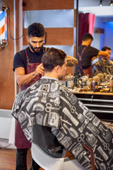 Master cuts hair and beard of men in the barbershop, hairdresser makes hairstyle for a young man