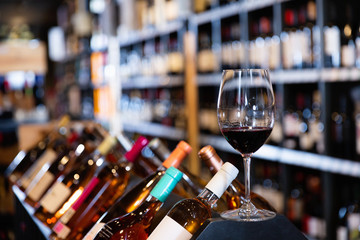 Closeup of red wine glass on blurred background with shelves in wine shop