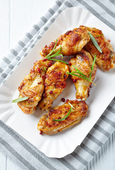 Roasted chicken wings with fresh rosemary on bright wooden background. Top view.