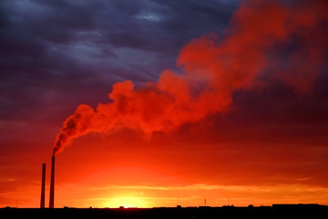 Colorful Magic Sunset. Roofs of city houses during sunrise. Birds flying in the sky. Dark smoke coming from the thermal power plant pipe.