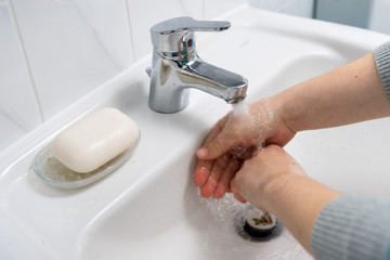 Two hands washing in a white sink