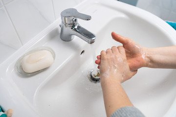 two hands washing with soap in a white sink