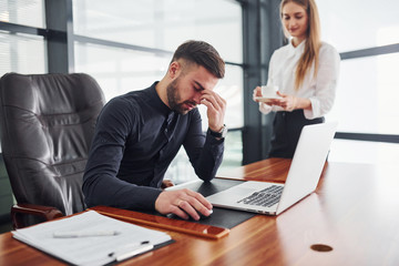 Guy feels bad. Woman and man in formal clothes working together indoors in the office by table