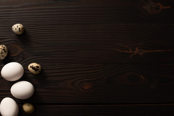 top view of white eggs and quail eggs on brown wooden background