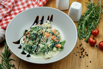 Stewed vegetables (carrots, broccoli and spinach) in cream sauce with dorblu cheese in a white pial on a wooden background. Close up view. Copy space