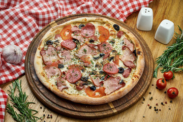 Pizza with salami, ham, olives, tomatoes, cheese and white sauce on a wooden tray. Pizza in composition with ingredients on a wooden table