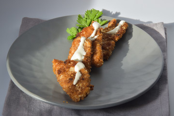 Deep-fried chicken pieces with white sauce and parsley on a gray plate. White background.