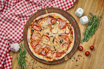 Pizza with ham, bell pepper, mushrooms, tomatoes, cheese and white sauce on a wooden tray. Pizza in composition with ingredients on a wooden table