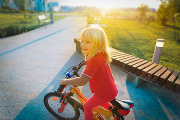 cute happy little girl riding bike at sunset