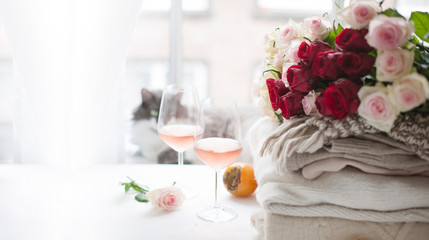 Bouquet of roses natural light. Flowers White and red roses by the window and two glasses of rose wine. Cozy and romantic atmosphere. Banner long format. Selective focus shifted from the subject.