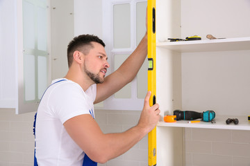 Worker measuring newly installed kitchen furniture indoors