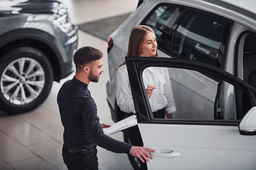 Woman choosing car by help of male assistant indoors in the salon