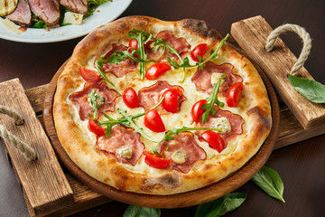 Pizza with ham, cheese, cherry tomatoes, arugula on a wooden tray. Close up. Italian cuisine