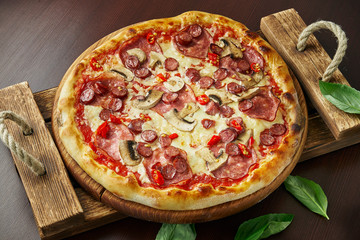 Pizza with pepperoni salami, melted cheese, mushrooms and chili pepper on a wooden tray. Close up. Italian cuisine