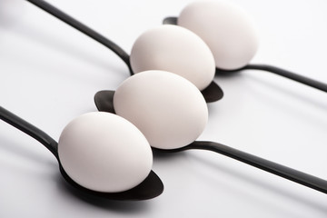 selective focus of chicken eggs on black spoons on white surface