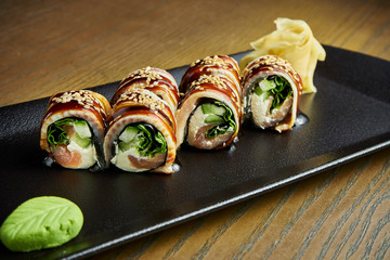 Fresh eel rolls with salmon, cucumber and Philadelphia cheese on a black plate on a wooden background. Japanese sushi roll