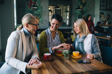 woman showing engagement ring to her friends while drinking coffee in cafeteria