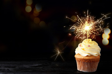 Birthday cupcake with sparkler on table against dark background. Space for text