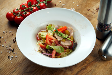 Appetizing warm salad with beef and fresh vegetables in white plate on wooden background. Healthy eating. Close up, copy space