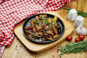 Baked potatoes smoked sausages, mushrooms in a pan on a wooden background. Close up, selective focus