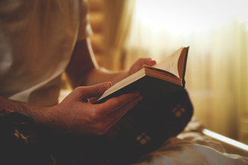 Young man reading book on bed at home, closeup