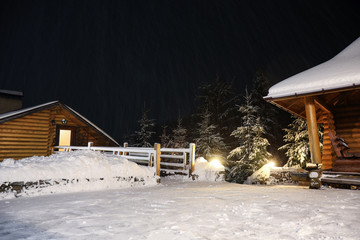 Wooden cottage and bridge covered with snow near fir forest at night. Winter vacation