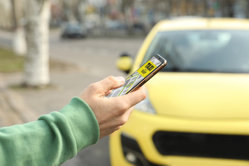 Man ordering taxi with smartphone on city street, closeup