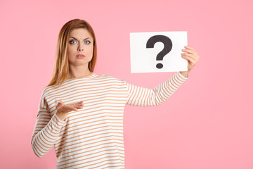 Confused woman holding question mark sign on pink background