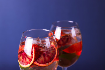 Summer lemonade, cocktail or sangria with red blood oranges and ice in glasses. Fresh citrus drink on blue background