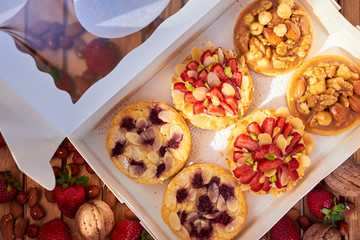 White paper box with six mini tart cupcakes. Tarts with with strawberries, nuts and blueberries. Top view