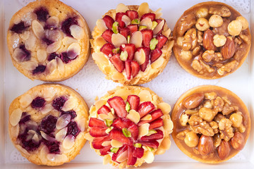 Top view on white paper box with six mini tart cupcakes. Tarts with with strawberries, nuts and blueberries. Close up