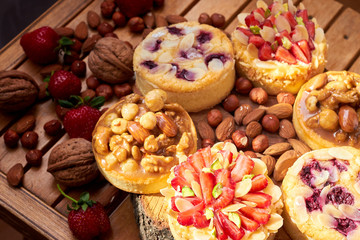 Mini tarts cupcakes with strawberries, walnuts, almond, nuts and blueberries on wooden background. Top view. Close up