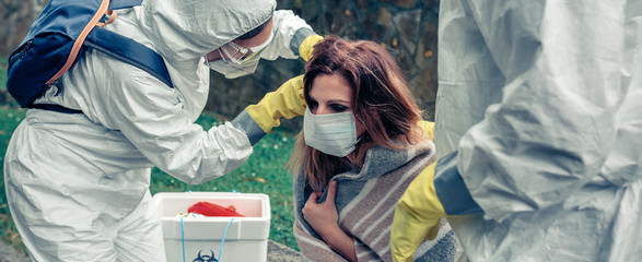 Obraz na płótnie Canvas Doctors putting protective mask on woman infected by a virus outdoors
