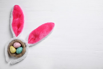 Headband with bunny ears, painted eggs and space for text on white wooden background, flat lay. Easter holiday