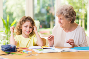 Smiling grandmother helping her cute grandson with homework after school