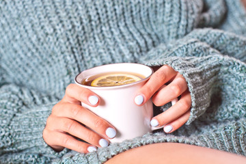 Female hands holding mug of hot tea with lemon in morning. Young woman relaxing tea cup on hand.