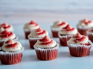 Red velvet mini cupcakes with cream cheese frosting on a white surface with a wood background.