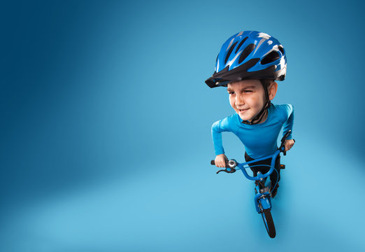 funny little boy with a bicycle in a helmet on a blue background. top view. studio photo