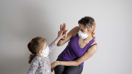 Little girl in protective mask is cheerfully knocks mother's hand, gives her five. Little daughter gives five to her mother. Parents spend spare time together with child.  Coronavirus or COVID19. 