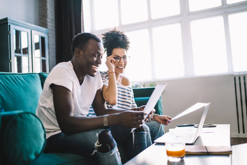 Multiethnic couple smiling on sofa with laptop