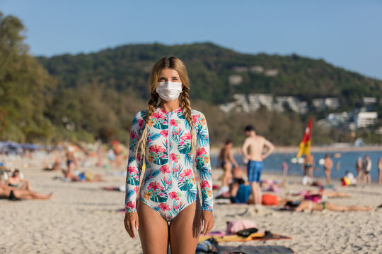 A woman and a child in a protective surgical mask on their face are standing on the beach in swimsuits. Chinese coronavirus disease COVID-19 is dangerous - Powered by Adobe