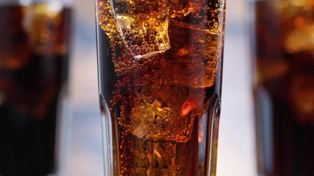 Closeup bubbles in glass with cola and ice cubes. Bubbles rise up of fizzy drink