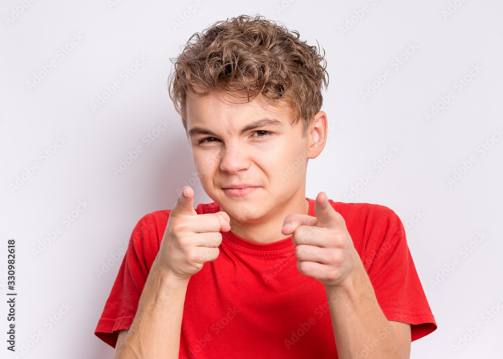 Poster Portrait of teen boy pointing fingers at camera, front view. Cute child in red t-shirt choose you, on grey background.