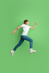Fototapeta na wymiar Shocked using phone in jump. Caucasian young woman's portrait isolated on green studio background. Beautiful female model in white shirt. Concept of human emotions, facial expression, sales, ad, youth