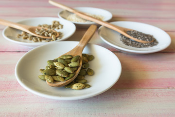 Various seeds in a wooden spoon on a wooden table.