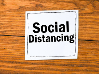 SOCIAL DISTANCING text on a white card and a wooden table.