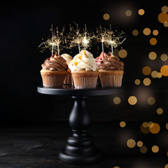 Birthday cupcakes with sparklers on wooden table against dark background