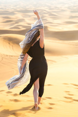 Caucasian young beautiful girl alone is in a hot, waterless desert. Runs along the sandy mountains and dunes A girl in a black long dress walks through the desert.