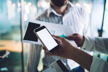 Coworkers browsing smartphone and holding documents in company